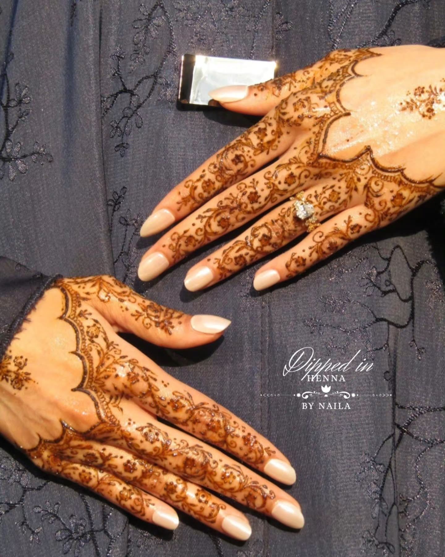 Two hands with scalloped henna on dark fabric