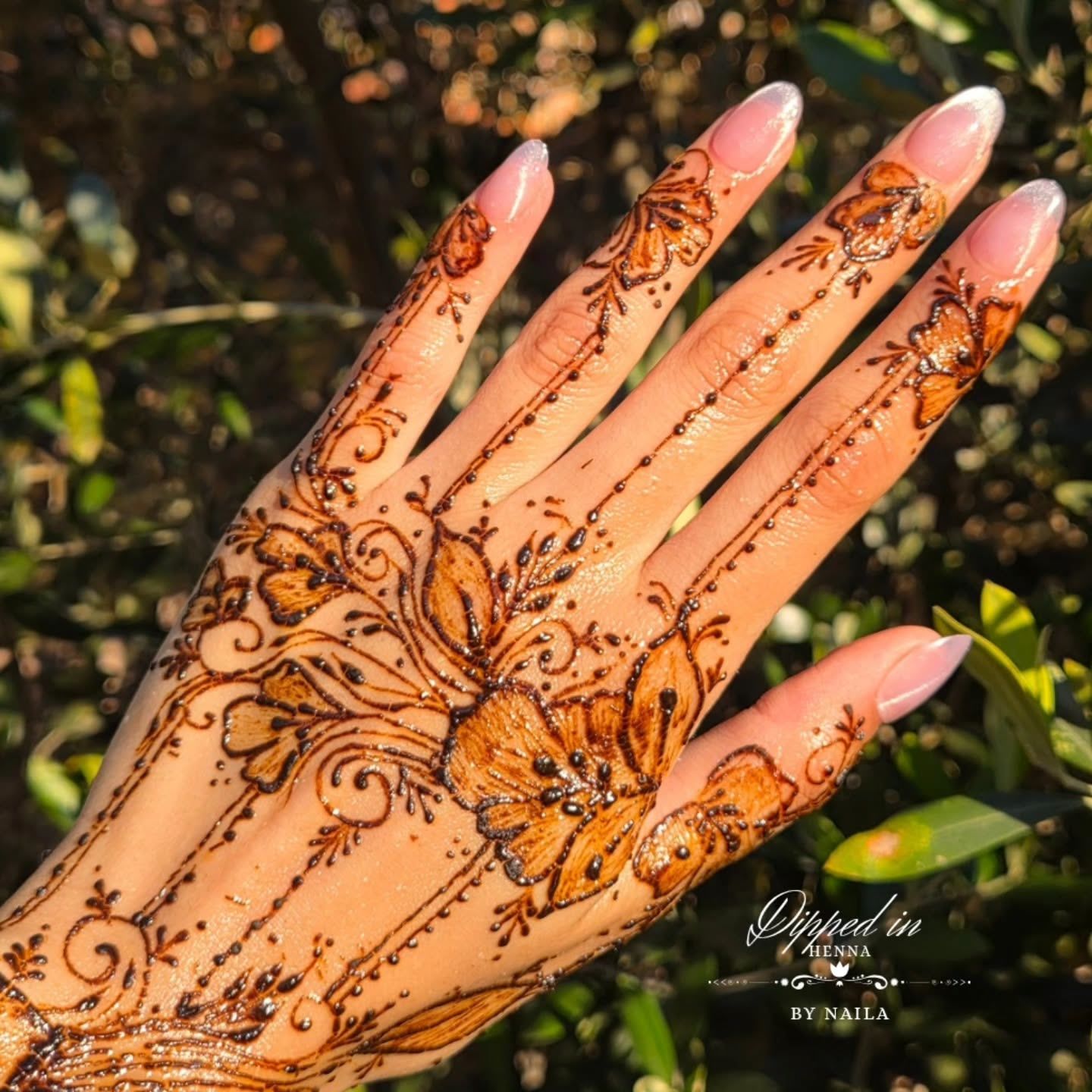 Orange floral henna on the fingers against green leaves